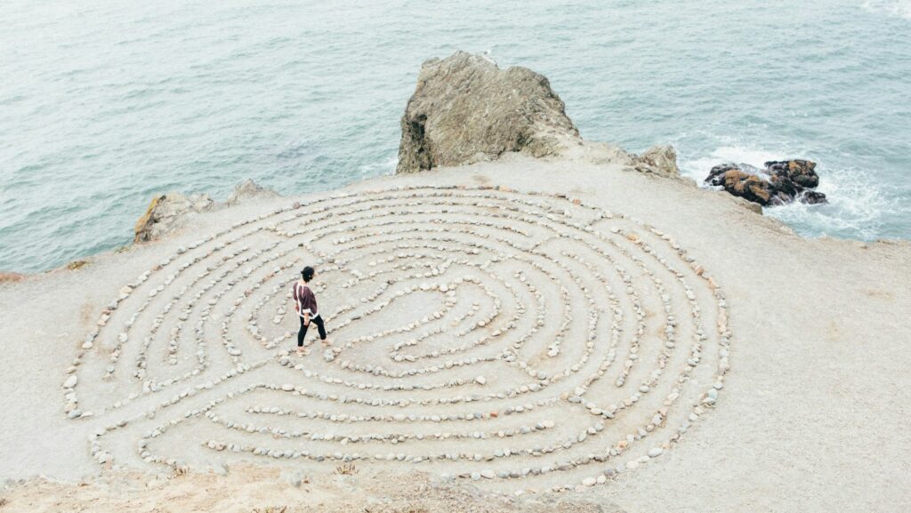 A person navigates a circular labyrinth made of stones on a sandy cliffside, with the ocean in the background—a true content hub for serene reflection.