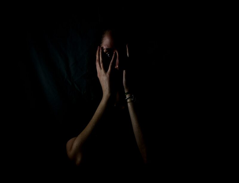 woman holding her face in dark room representing a stressful situation after dismissal after employee followed correct procedures and policies