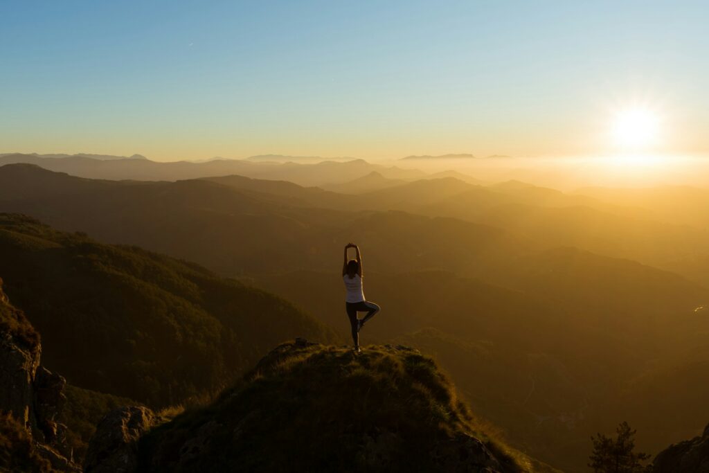 woman stretching on mountain top during sunrise: are we taking wellbeing too far?