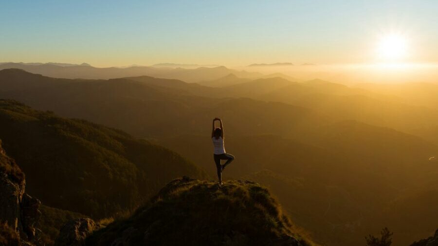 woman stretching on mountain top during sunrise: are we taking wellbeing too far?