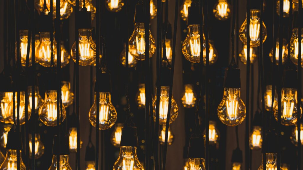 Numerous incandescent light bulbs hang illuminated against a dark background, creating an atmosphere that reflects the brilliance of collaboration.