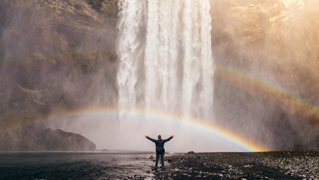 person in front of waterfalls with double rainbow during daytime