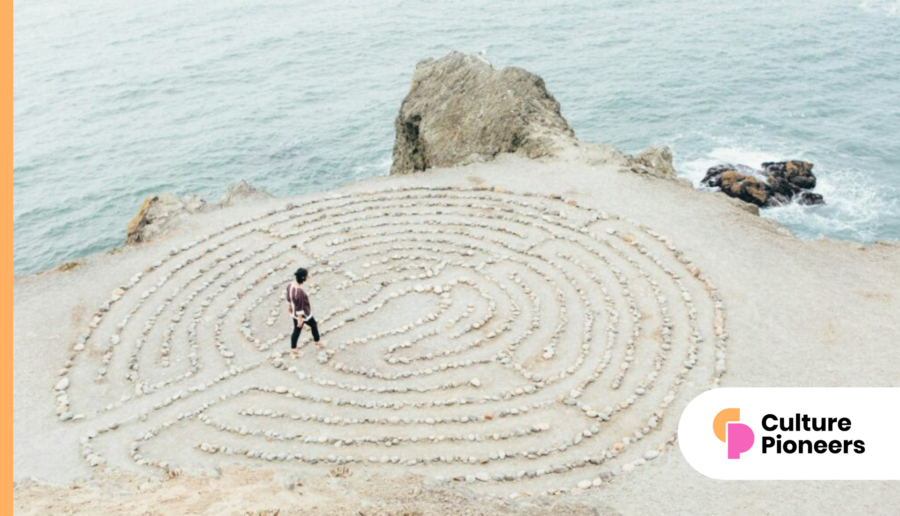 A person navigates a circular stone labyrinth on a rocky coastal cliff, contemplating the ebb and flow of culture in the workplace as the ocean whispers its timeless wisdom below.