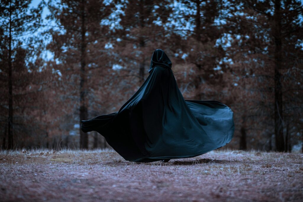 a woman in a black cloak is walking through the woods, The Traitors