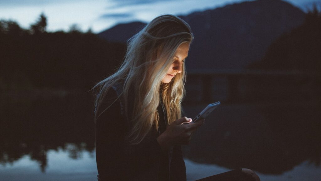 technostress, woman looking at phone beside body of water