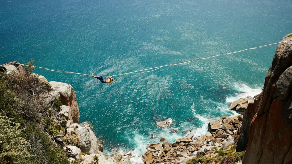 A daring highliner gracefully balances on a tightrope over a scenic turquoise ocean cliff.