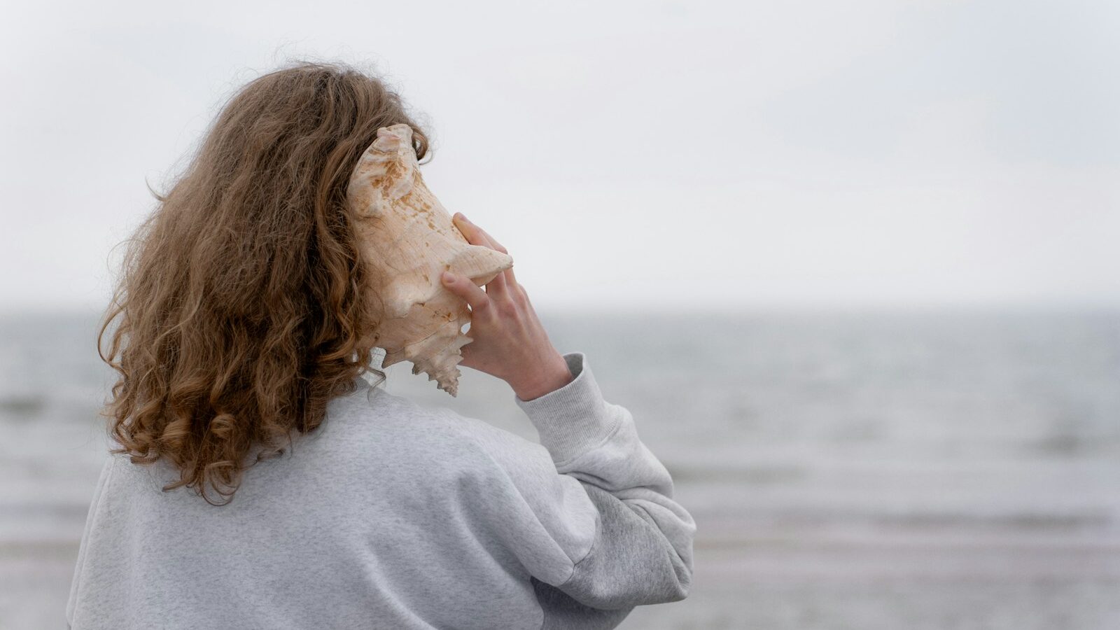 a woman holding a seashell up to her face, representing the QUIET Listening Framework