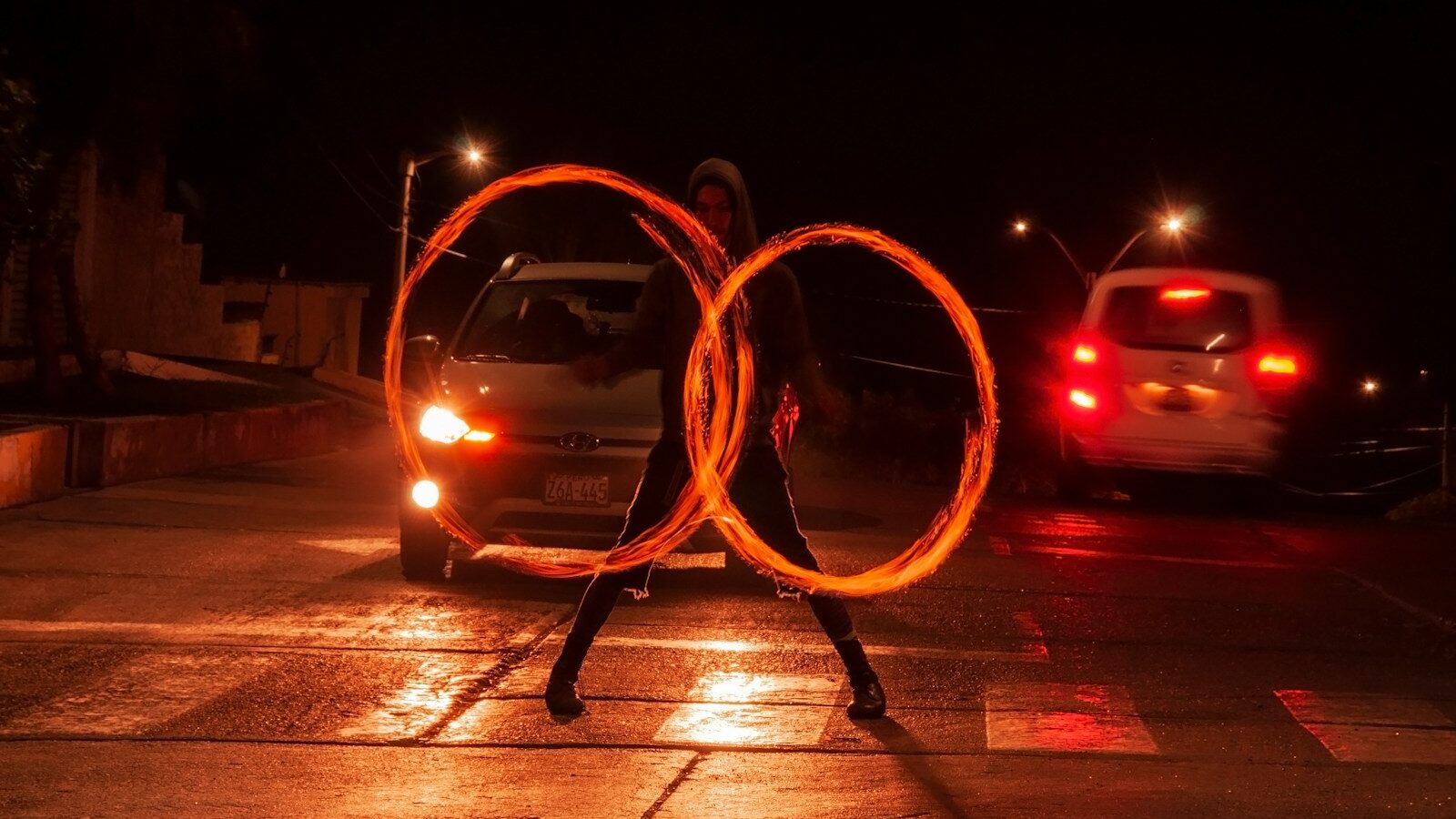 a man holding two fire hoopes in front of a car, depicting HR juggling two jobs