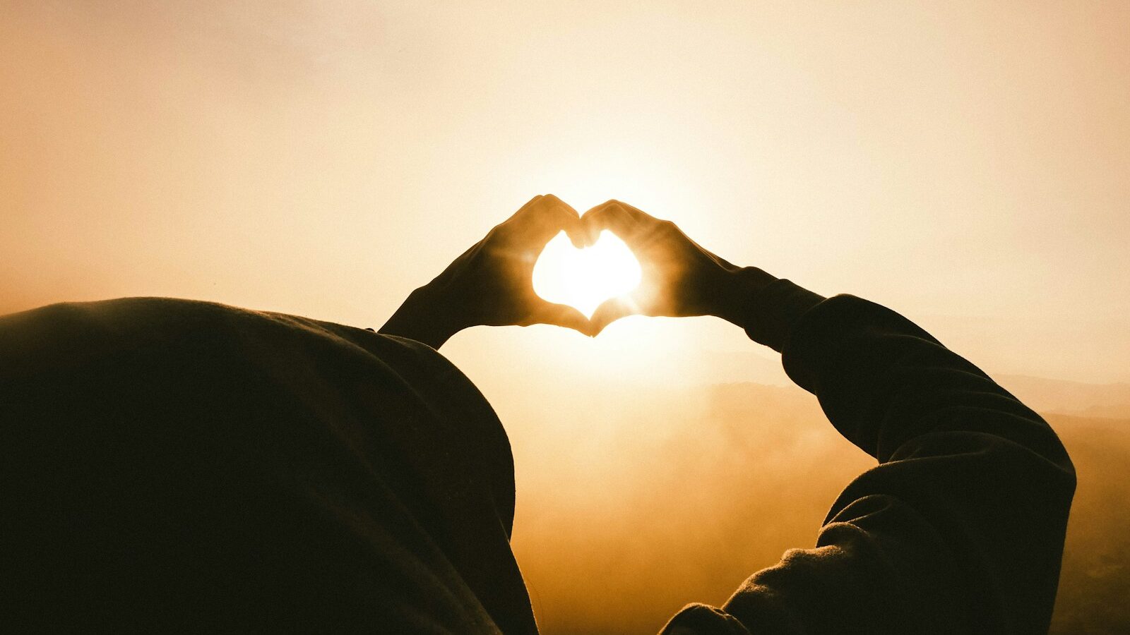 person doing heart shape hand with sun light passing through.