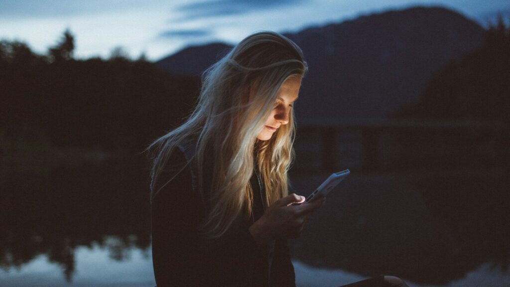 woman looking at phone beside body of water