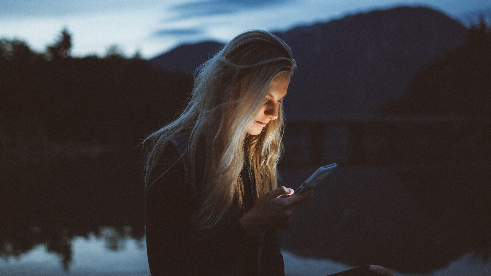 woman looking at phone beside body of water